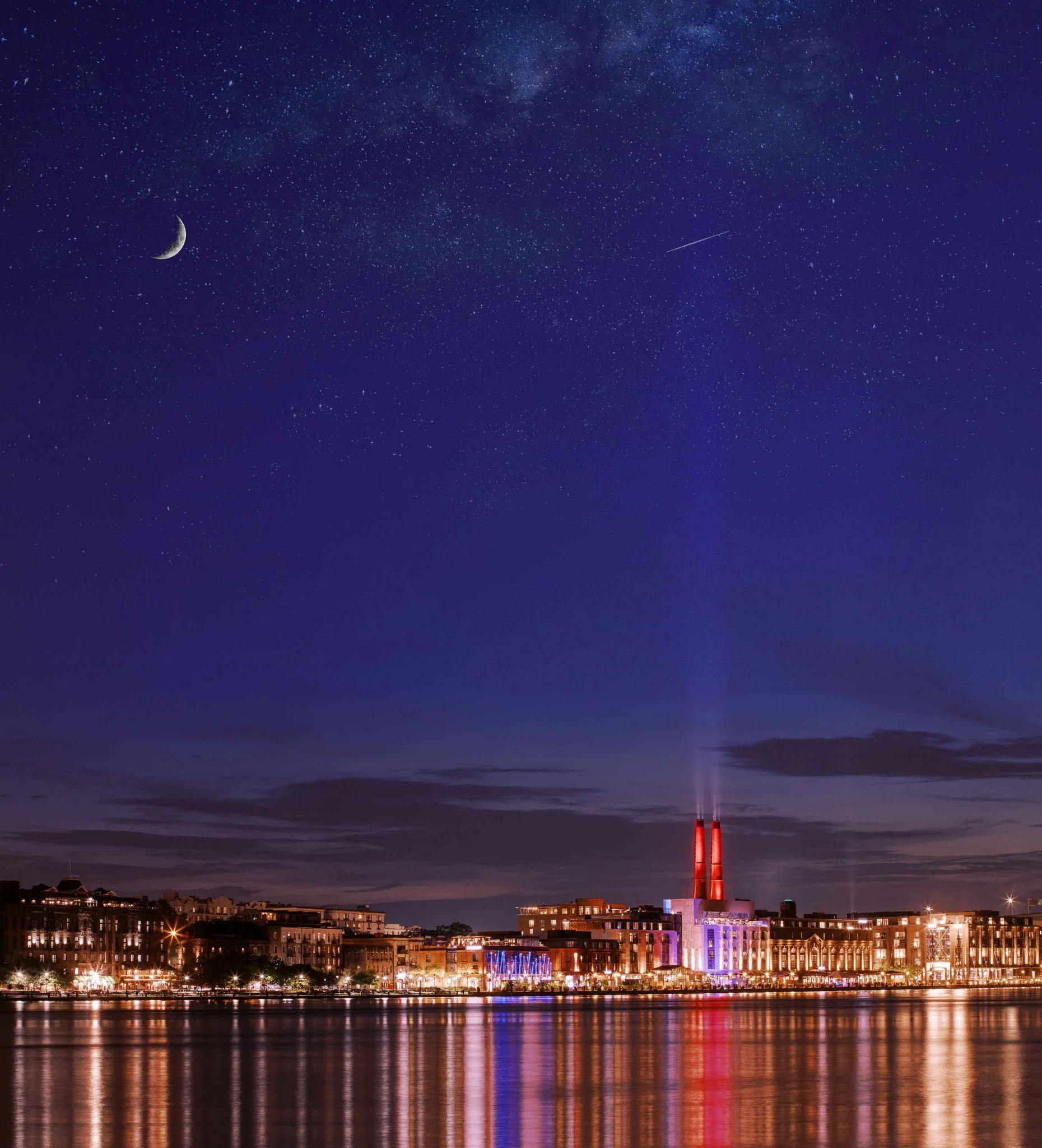 A crescent moon over the city and river at blue hour