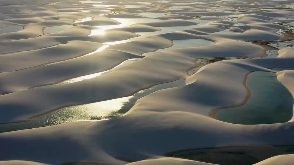 Aerial film still of sculpted dunes and lagoons in Lençóis Maranhenses