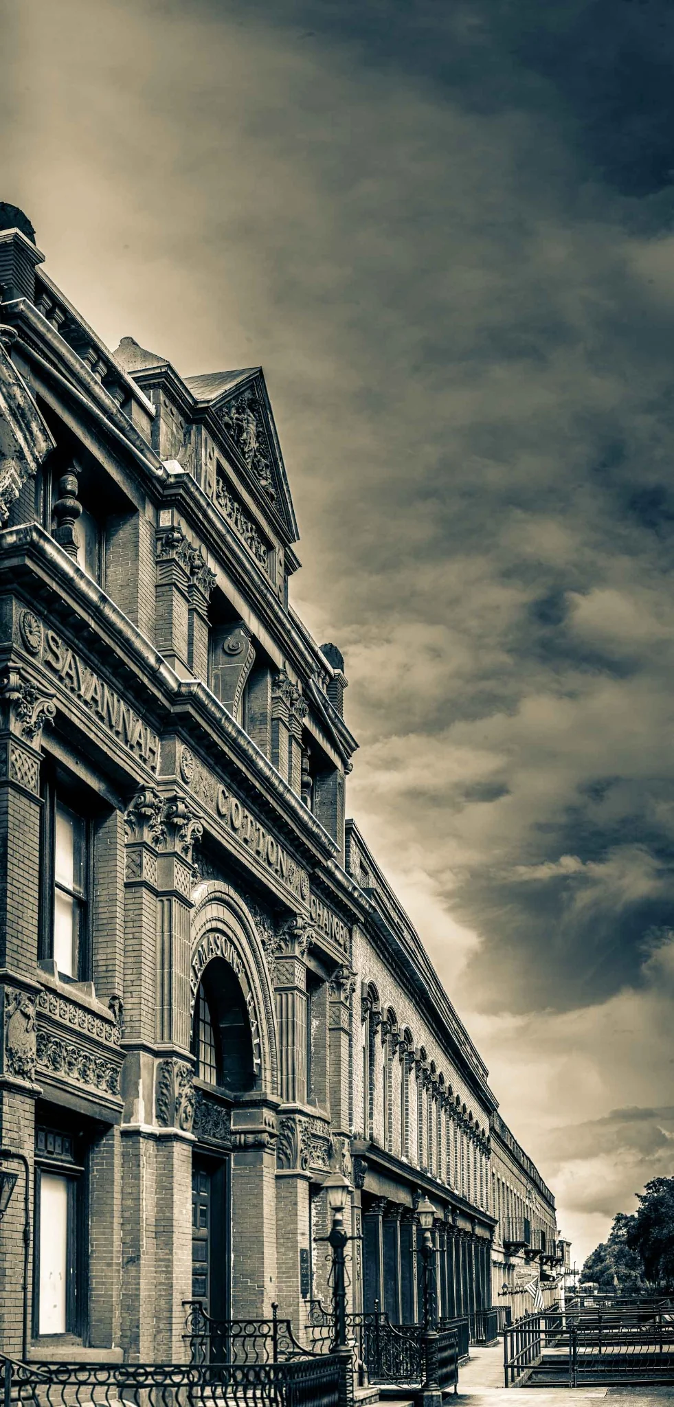 Tall stone building facade receding along a street beneath a dramatic sky.